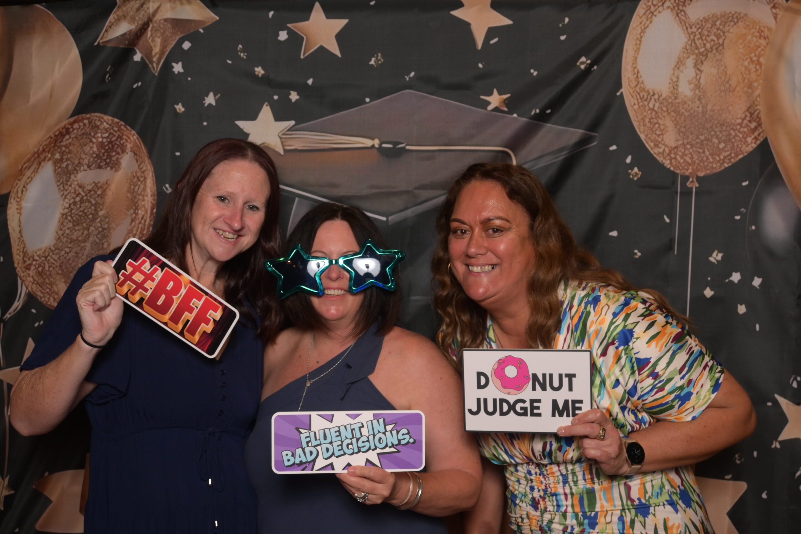 Graduates celebrating with props in front of the photo booth backdrop